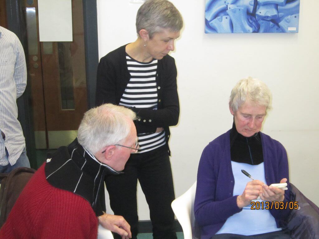 A lady with MND wearing a prototype collar communicates to other group members via notepad and pen.